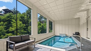 A modern indoor swimming pool with a view of lush greenery outside.