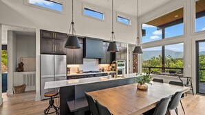 A modern kitchen with a large island, dark cabinets, stainless steel appliances, and a dining area with a wooden table and chairs.