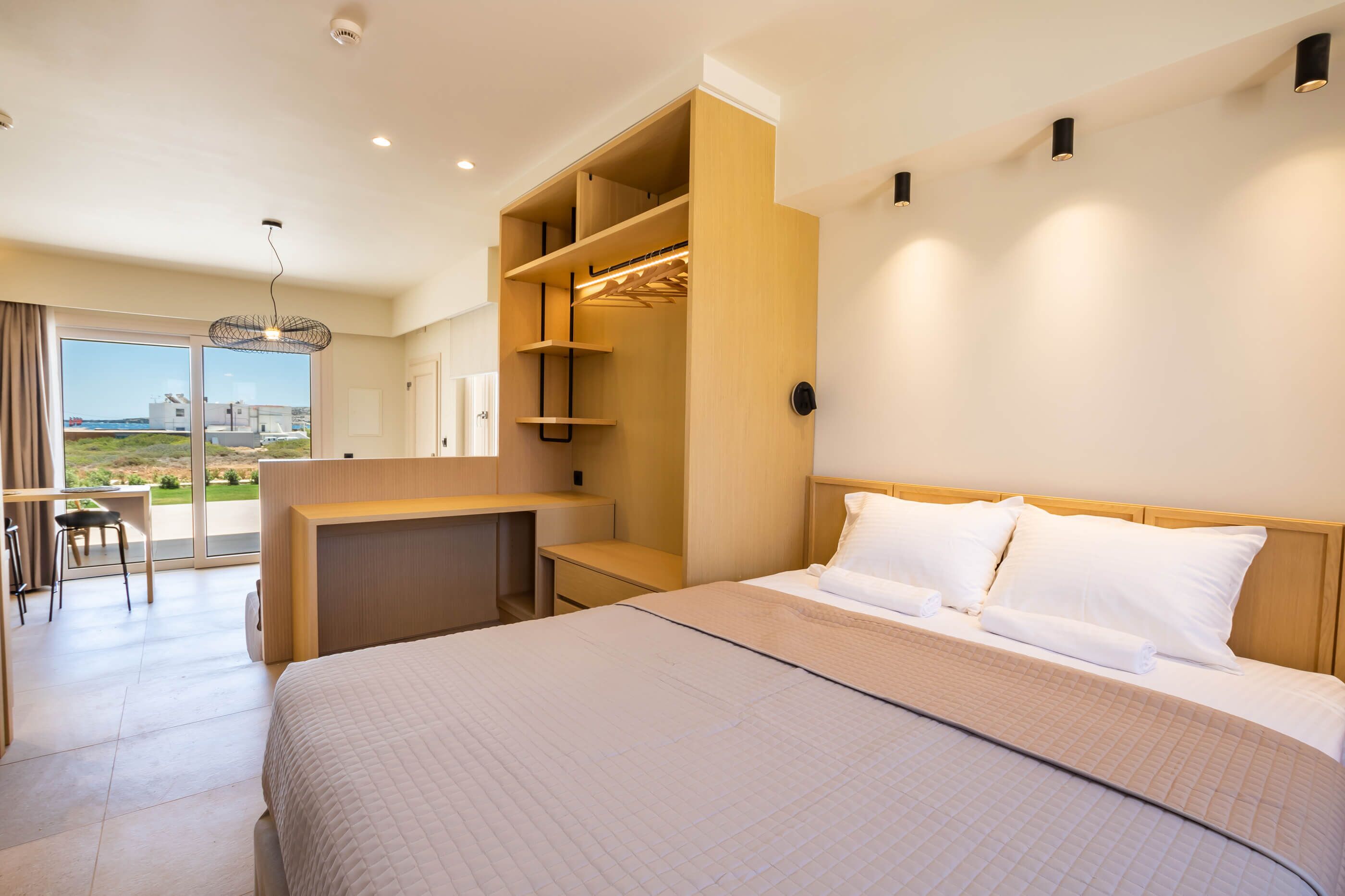 A modern hotel room with a large bed, built-in closet, desk, and a balcony with a view.