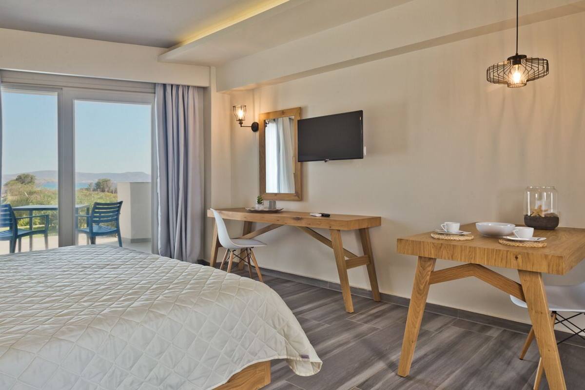 A hotel room with a bed, a desk, a chair, a TV, and a table with a cup and saucer.
