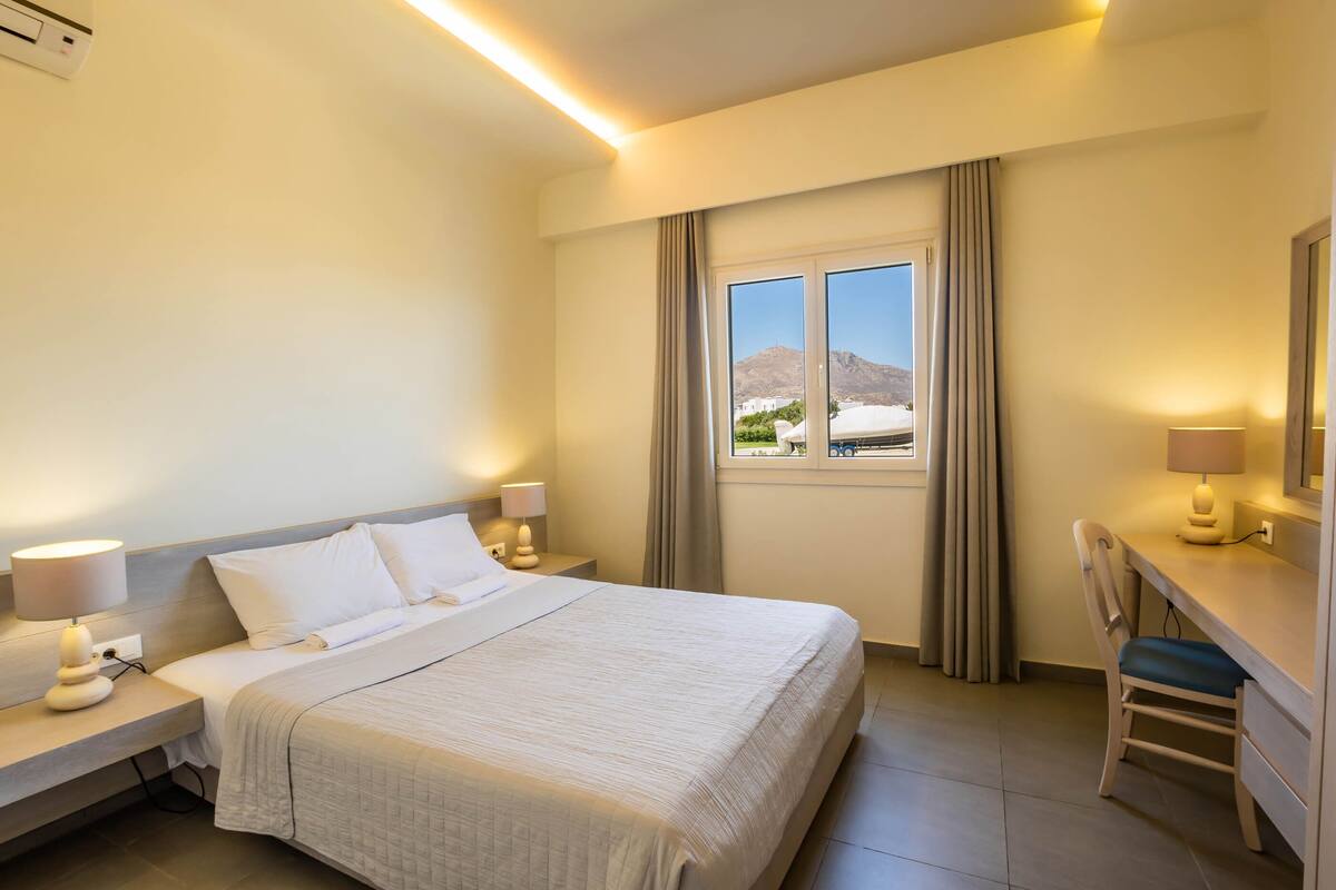 A hotel room with a bed, bedside tables, a desk, and a window with curtains.