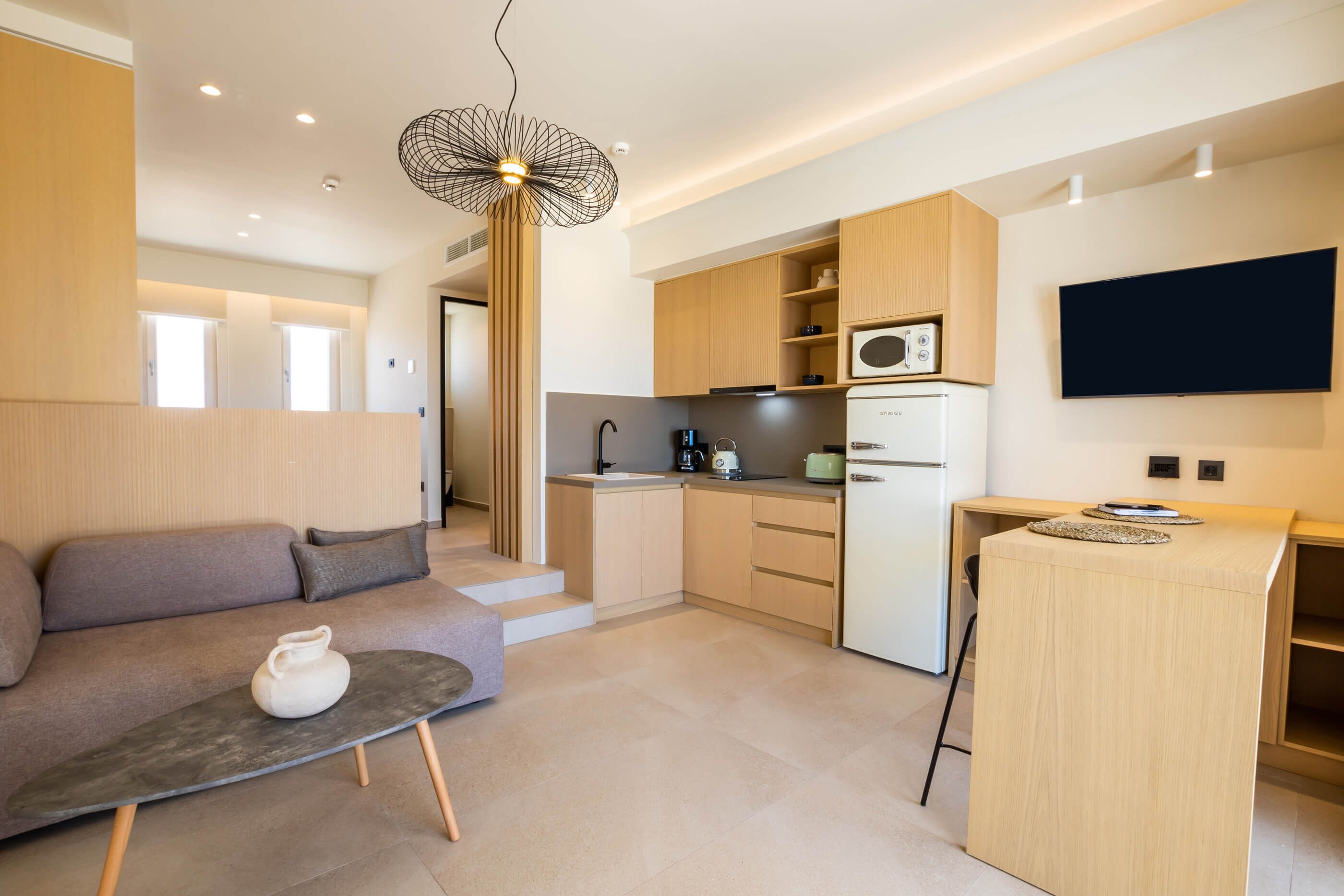 Eine moderne Küche mit Holzschränken, einer eingebauten Mikrowelle und einem Kühlschrank. Im Wohnbereich steht ein graues Sofa mit einer weißen Vase auf einem kleinen Tisch.