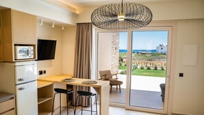 A compact kitchen with a built-in microwave, a dining area with a table and chairs, and a sliding glass door leading to a balcony with a view of the sea. - Thalassa Suites (Karpathos)