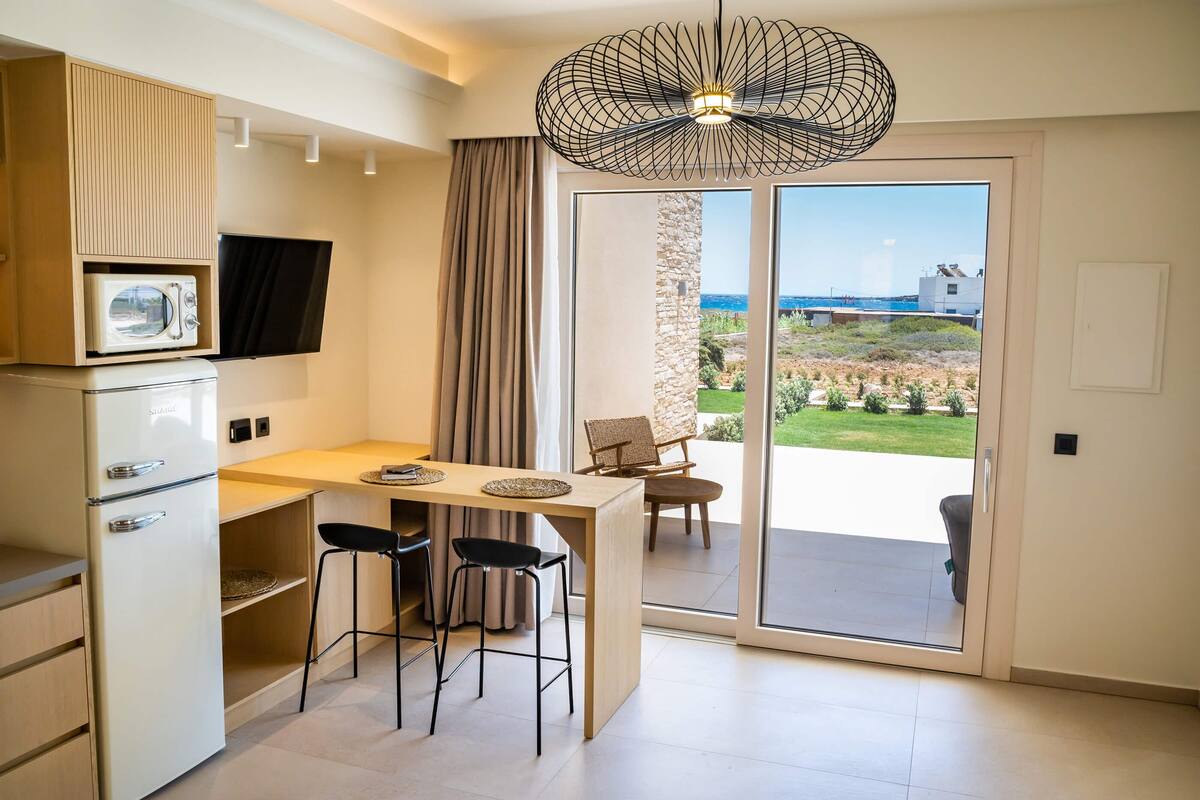 A compact kitchen with a built-in microwave, a dining area with a table and chairs, and a sliding glass door leading to a balcony with a view of the sea.