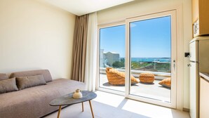 A modern living room with a sofa, a small table, and a view of the sea through large glass doors. - Thalassa Suites (Karpathos)