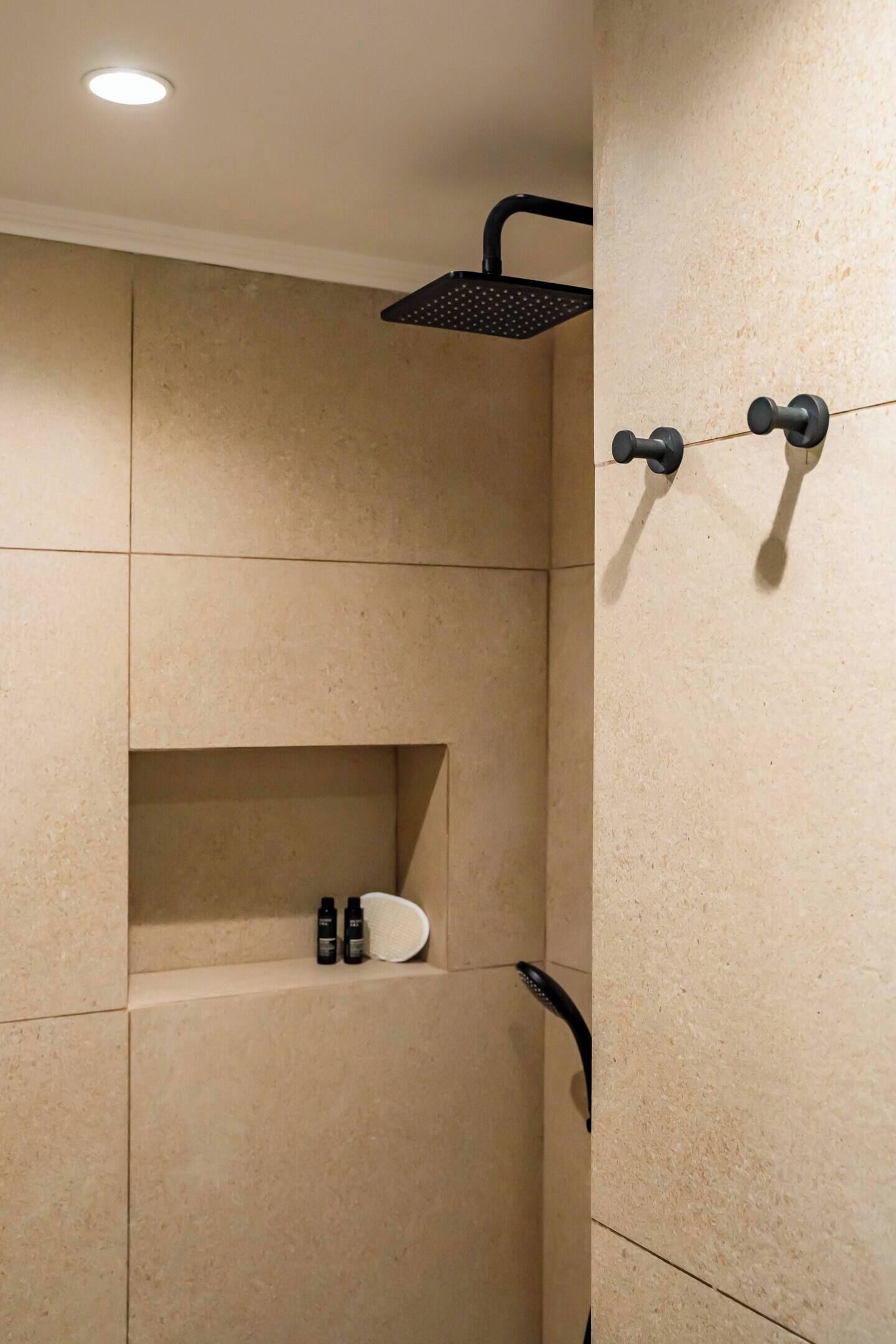 A modern shower with a black showerhead and a wall-mounted control panel.