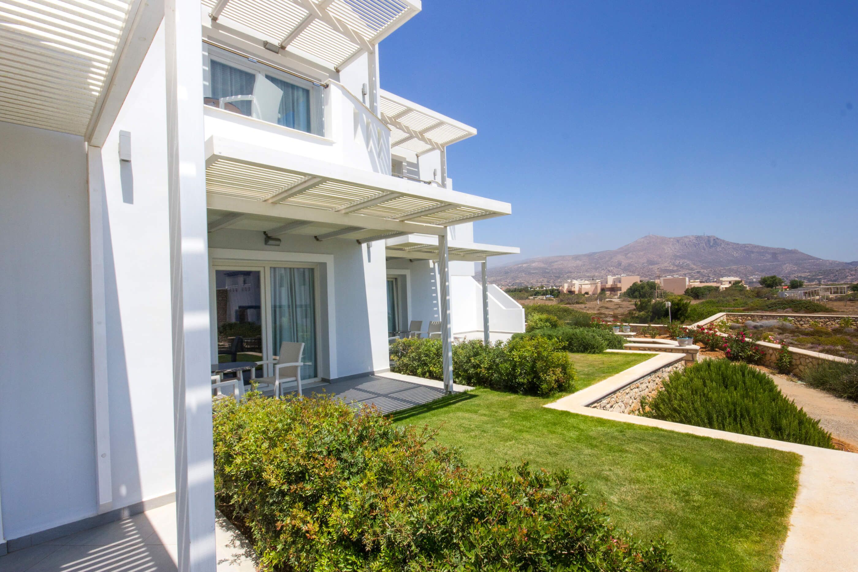 A modern white building with a balcony, a well-maintained lawn, and a mountainous backdrop.