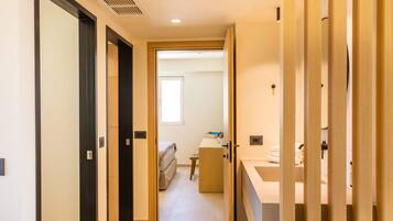 A narrow hallway with a bed, a desk, and a bathroom with a sink and mirror.