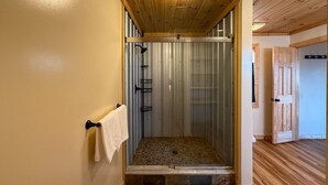 A shower with a wooden ceiling and a metal door, a towel hanging on a hook, and a wooden floor. - Spectacular Mountain Views Near Dollywood (Sevierville)