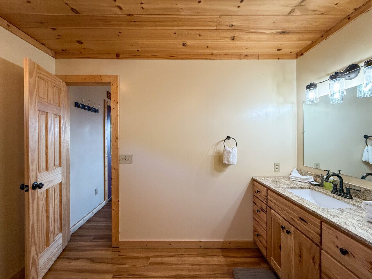 Een badkamer met houten vloeren, een houten wastafelmeubel met een wastafel en een spiegel met verlichting.