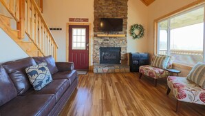 A cozy living room with a stone fireplace, wooden staircase, and a red door. - Spectacular Mountain Views Near Dollywood (Sevierville)