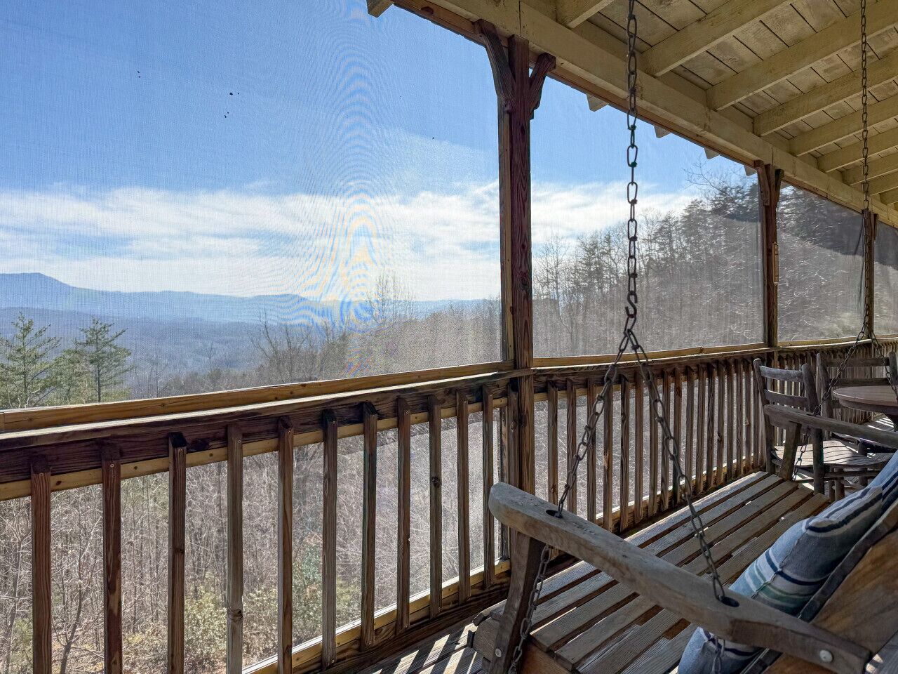 Eine Holzterrasse mit Schaukelstuhl und Tisch, mit Blick auf eine gebirgige Landschaft.