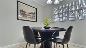 Un coin repas avec une table ronde, quatre chaises noires, une plante en pot et un tableau encadré au mur.