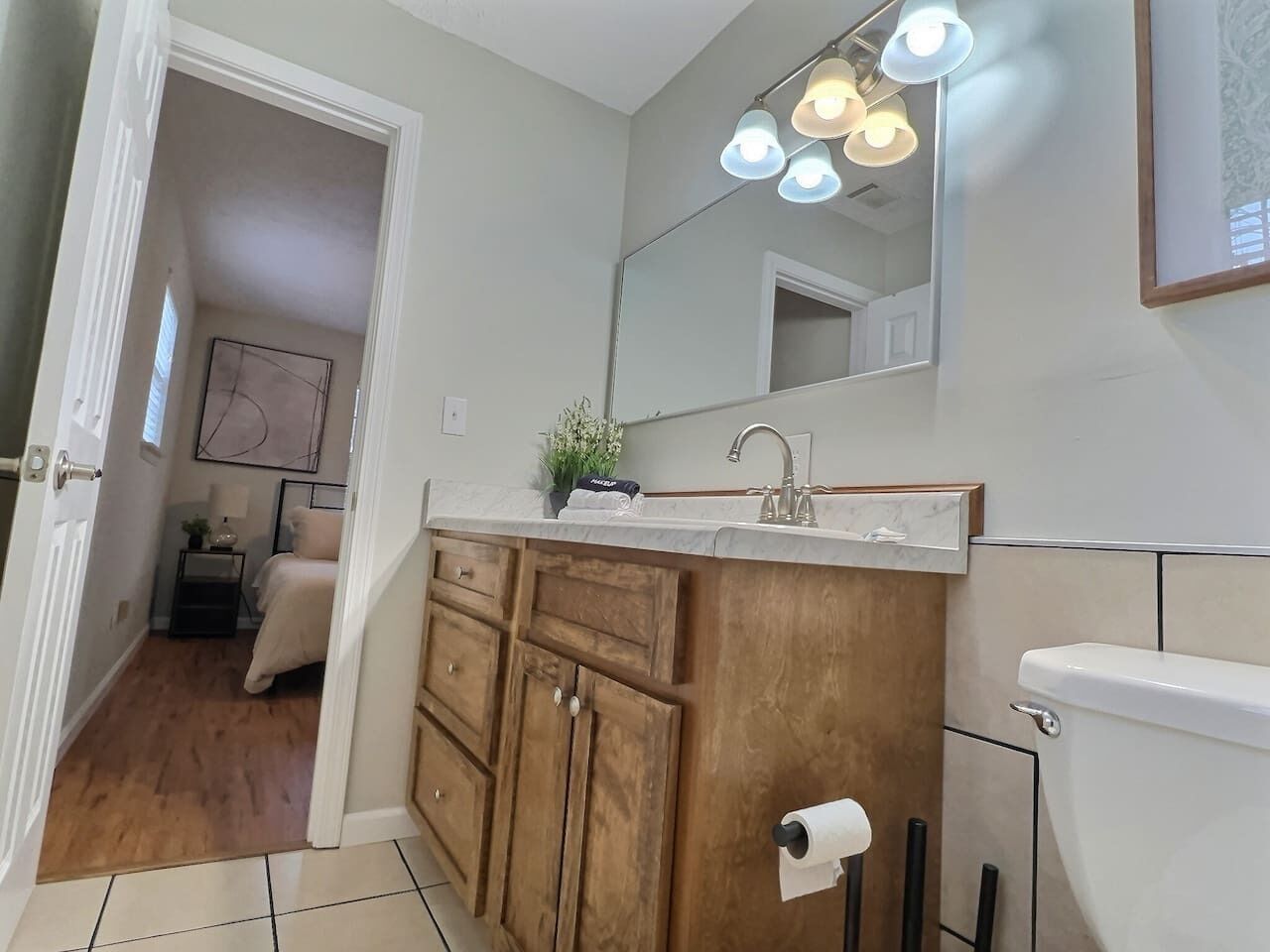A bathroom with a wooden vanity, a sink, and a toilet. There is a mirror above the vanity and a light fixture above the sink.