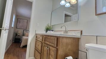A bathroom with a wooden vanity, a sink, and a toilet. There is a mirror above the vanity and a light fixture above the sink.