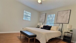 Une chambre à coucher avec un grand lit, un banc, deux tables de chevet et des œuvres d’art accrochées aux murs.