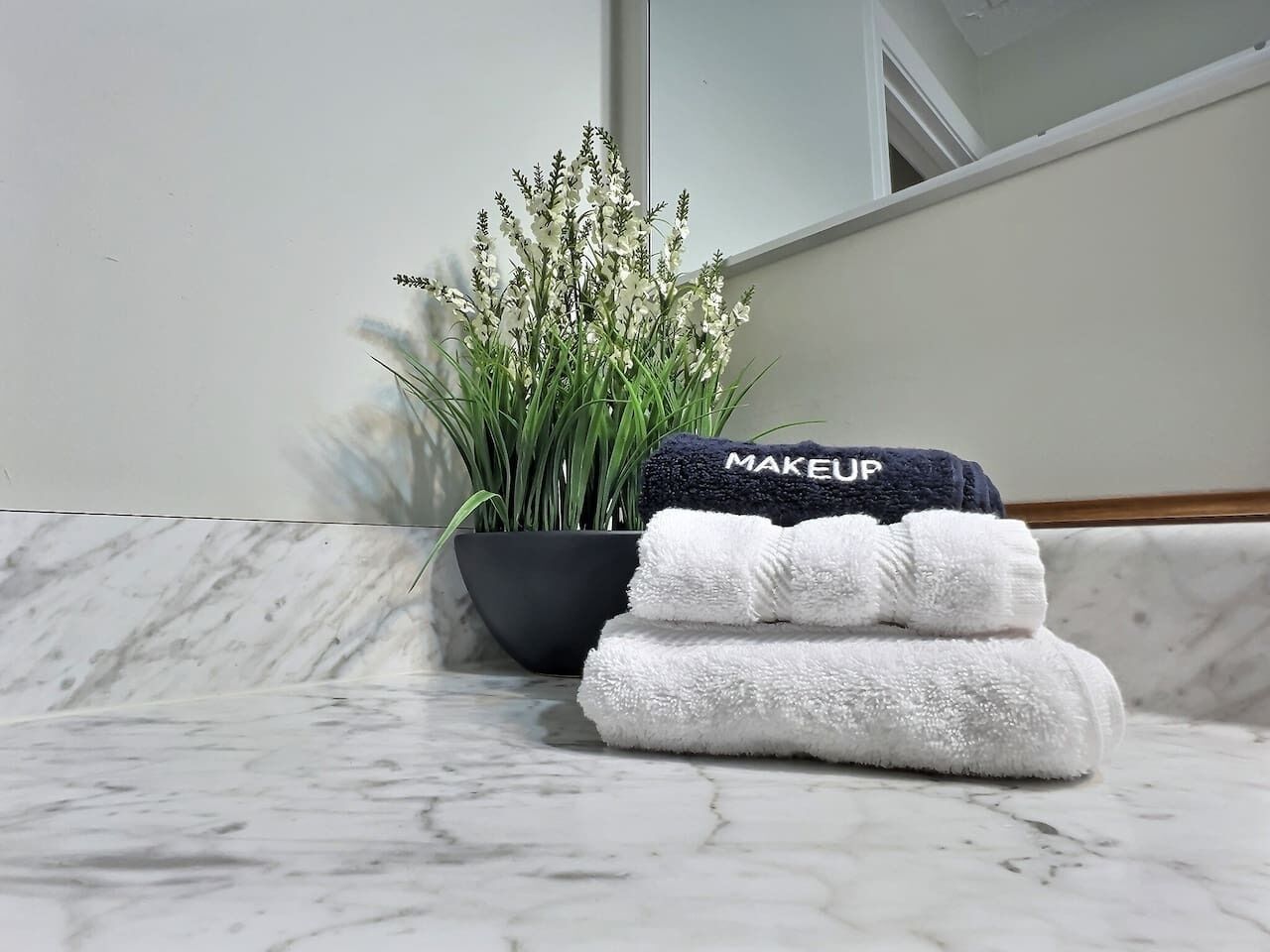 A bathroom with a marble countertop, a potted plant, and a stack of towels.