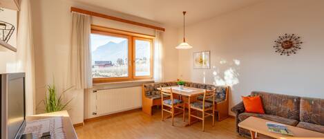 Una sala de estar con una mesa de madera, sillas, un sofá, un televisor y una ventana con vistas a la montaña.