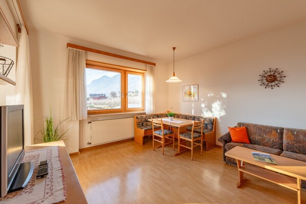 A living room with a wooden table, chairs, a sofa, a TV, and a window with a mountain view.