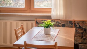 Un espace repas comprenant une table, des chaises, un luminaire suspendu et une vue sur l’extérieur à travers une fenêtre ornée de rideaux.