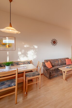 A dining area with a wooden table and chairs, a sofa with cushions, and a hanging light fixture.