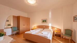 Une chambre d’hôtel avec un lit en bois, un bureau, une chaise, une armoire et un miroir.