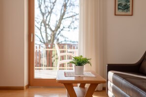 Una habitación con una mesa de madera, una planta en maceta, un sofá de cuero marrón y vistas a un espacio exterior con un árbol y una valla.