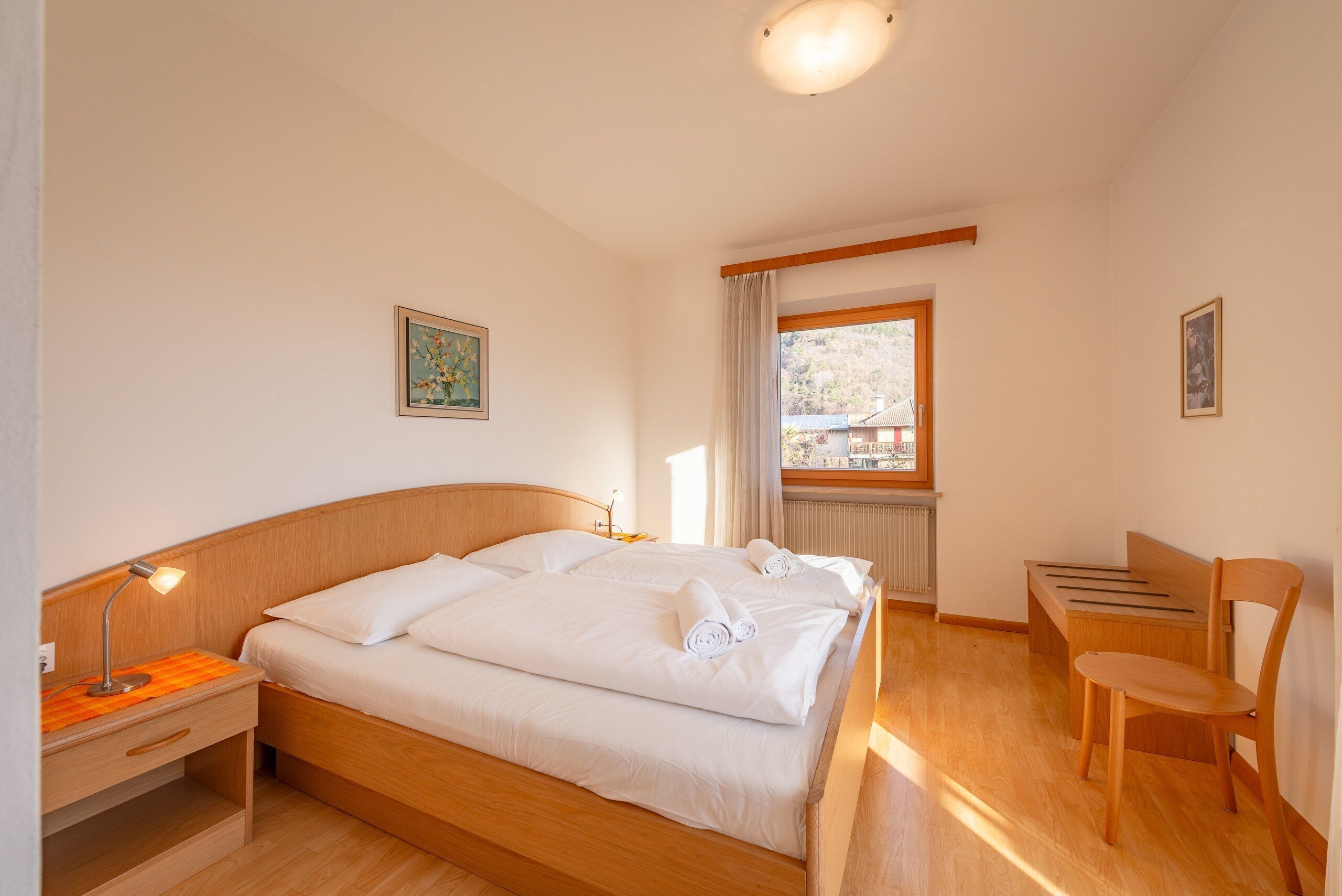 A hotel room with a wooden bed, a desk, a chair, and a window with a view of a building.