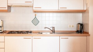 Uma cozinha com armários brancos, fogão a gás, pia e chaleira.
