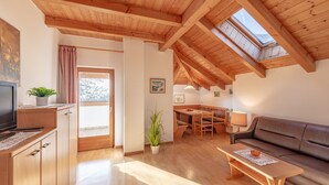 Uma sala de estar acolhedora com teto de madeira, um sofá, uma mesa de centro, uma televisão e um espaço de jantar com uma mesa e cadeiras.