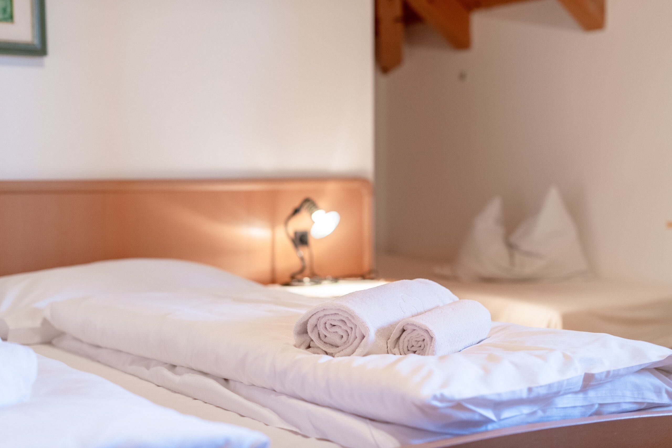 Ein ordentlich bezogenes Bett mit aufgerollten Handtüchern, einer Nachttischlampe und Kissen.