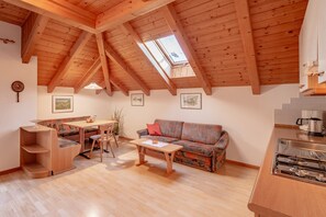 Un espacio habitable tipo loft acogedor con techo alto, vigas de madera, zona de comedor, sofá y kitchenette.