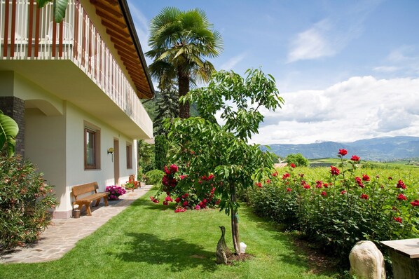 A house with a balcony, a garden with roses, and a view of mountains.
