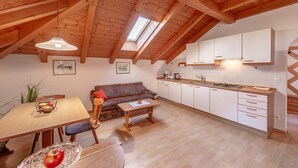 A cozy kitchen with wooden beams, a dining area with a table and chairs, and a sofa.