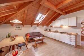 A cozy kitchen with wooden beams, a dining area with a table and chairs, and a sofa.