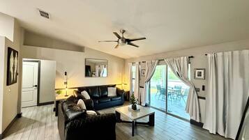 A living room with a black leather sofa, a coffee table, a ceiling fan, and a view through large sliding glass doors.
