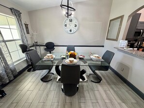 A dining area with a glass table, black chairs, and a wall clock.