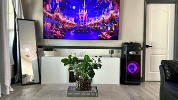 A living room with a flat-screen TV displaying a festive scene, a coffee table with a book, a plant, and a speaker.