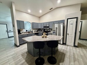 Una cocina moderna con encimeras de granito, electrodomésticos de acero inoxidable y una isla central con taburetes de bar.