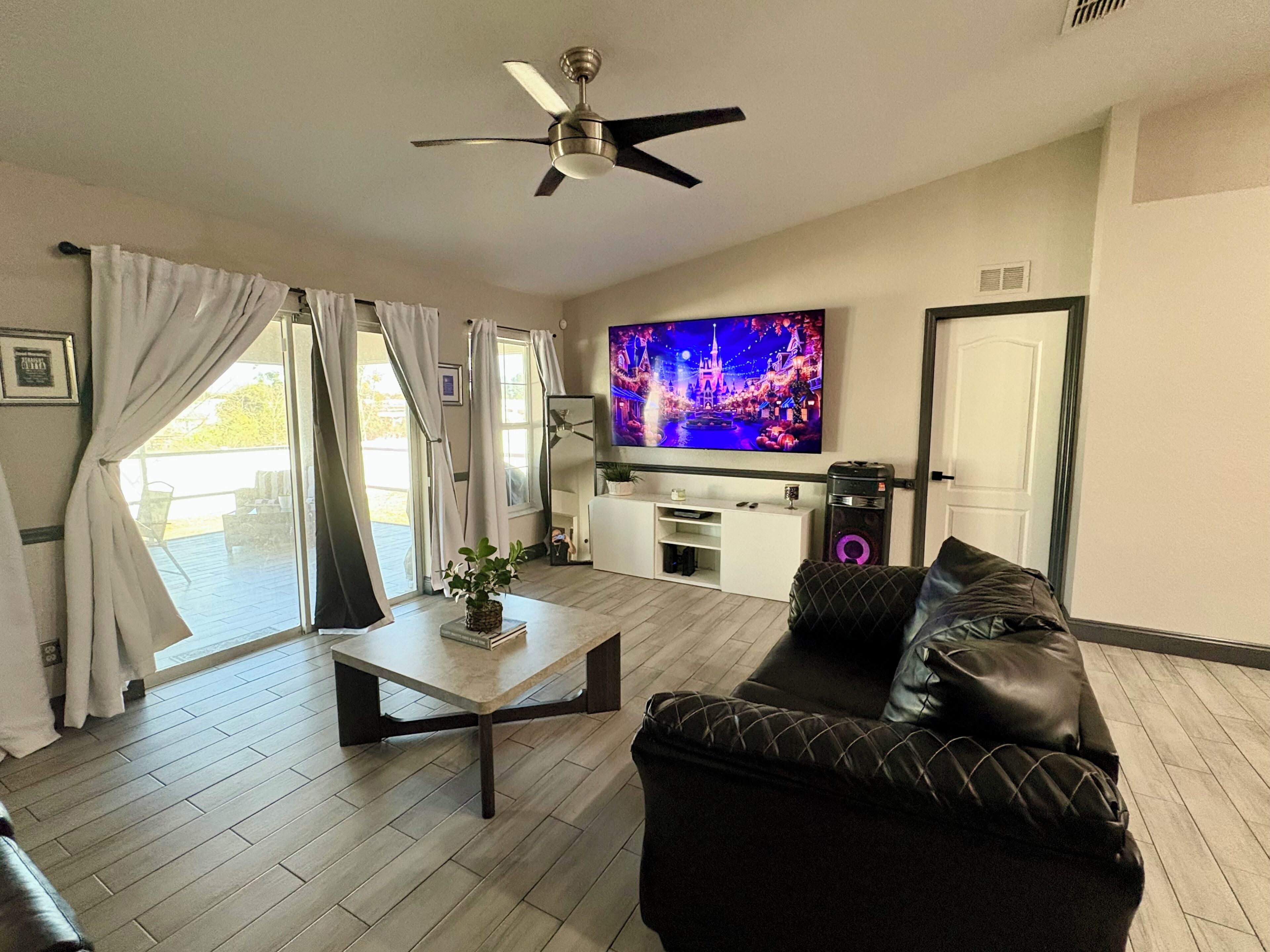A living room with a sofa, coffee table, TV, and a ceiling fan.