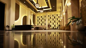 A spacious lobby with a reflective floor, a black sofa, decorative lighting, and a patterned wall.