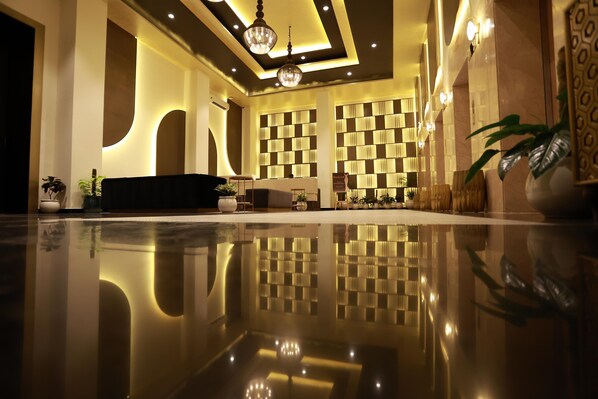 Un hall espacioso con suelo reflectante, un sofá negro, iluminación decorativa y un papel tapiz estampado.