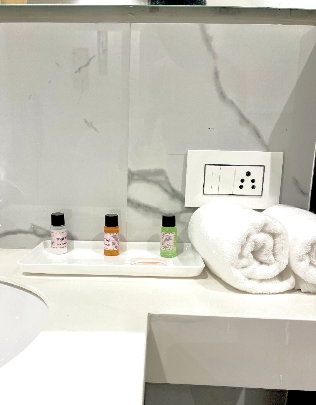 Ein Badezimmer mit einer weißen Ablage, drei Toilettenartikeln und zwei aufgerollten Handtüchern.