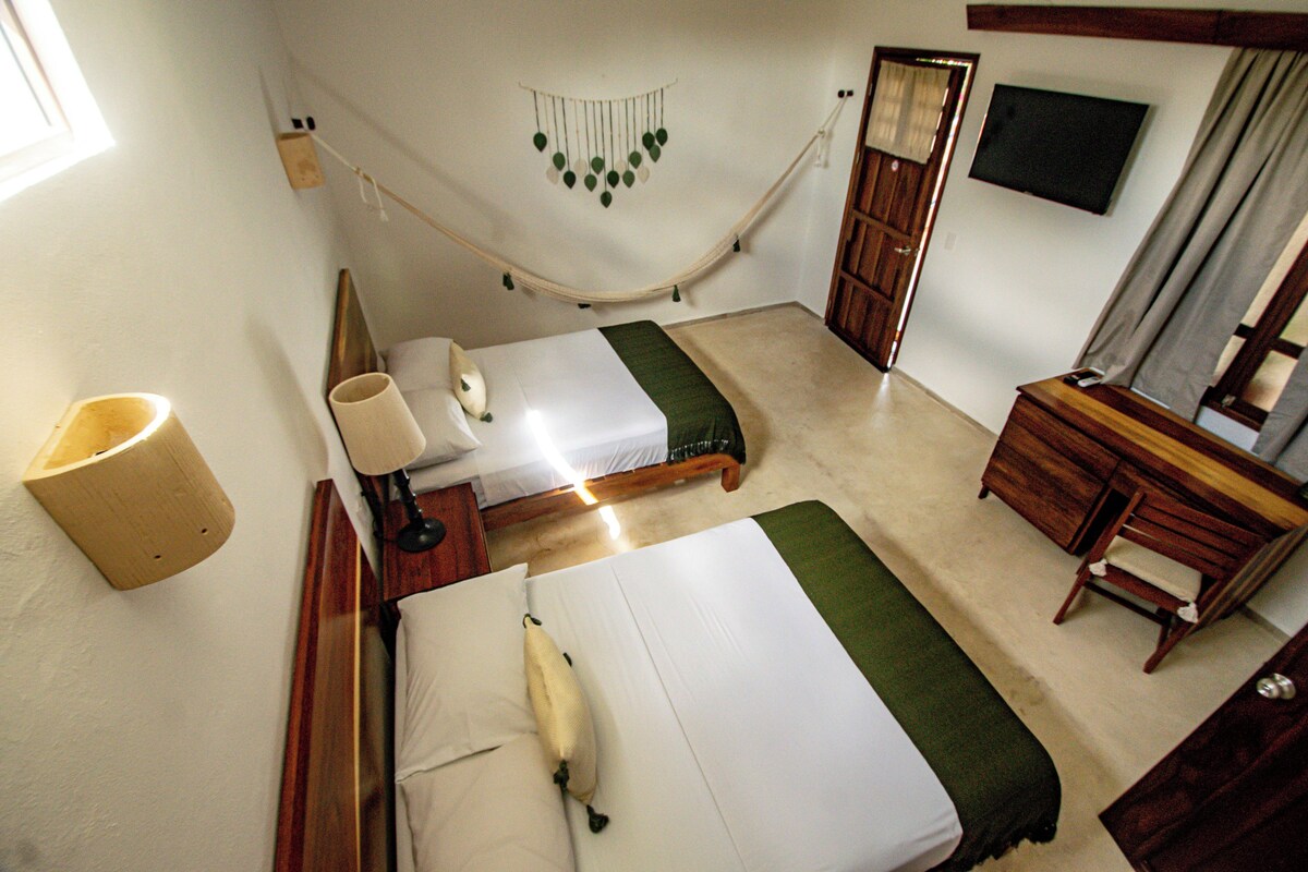 Een kamer met twee bedden, een houten dressoir, een bureau, een stoel, een hangmat en een televisie.