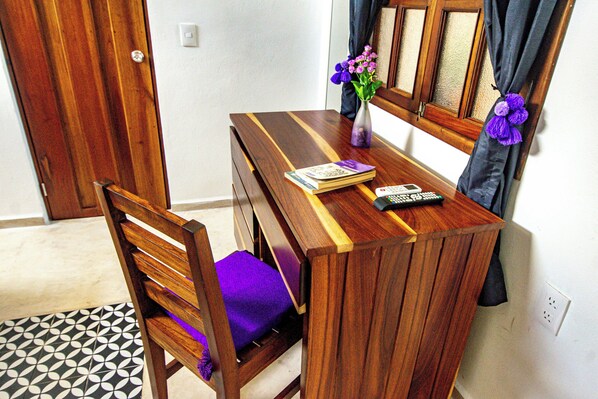 A wooden dining table with a purple cushion, a vase with purple flowers, and a remote control. - Hotel Boutique Kiin Wayeb (Valladolid)