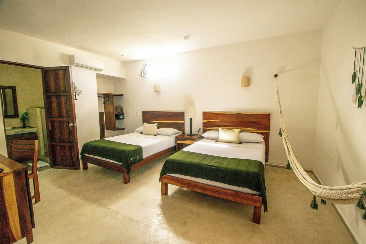 Habitación de hotel con dos camas individuales, un escritorio de madera, una silla, una lámpara de escritorio y una hamaca.