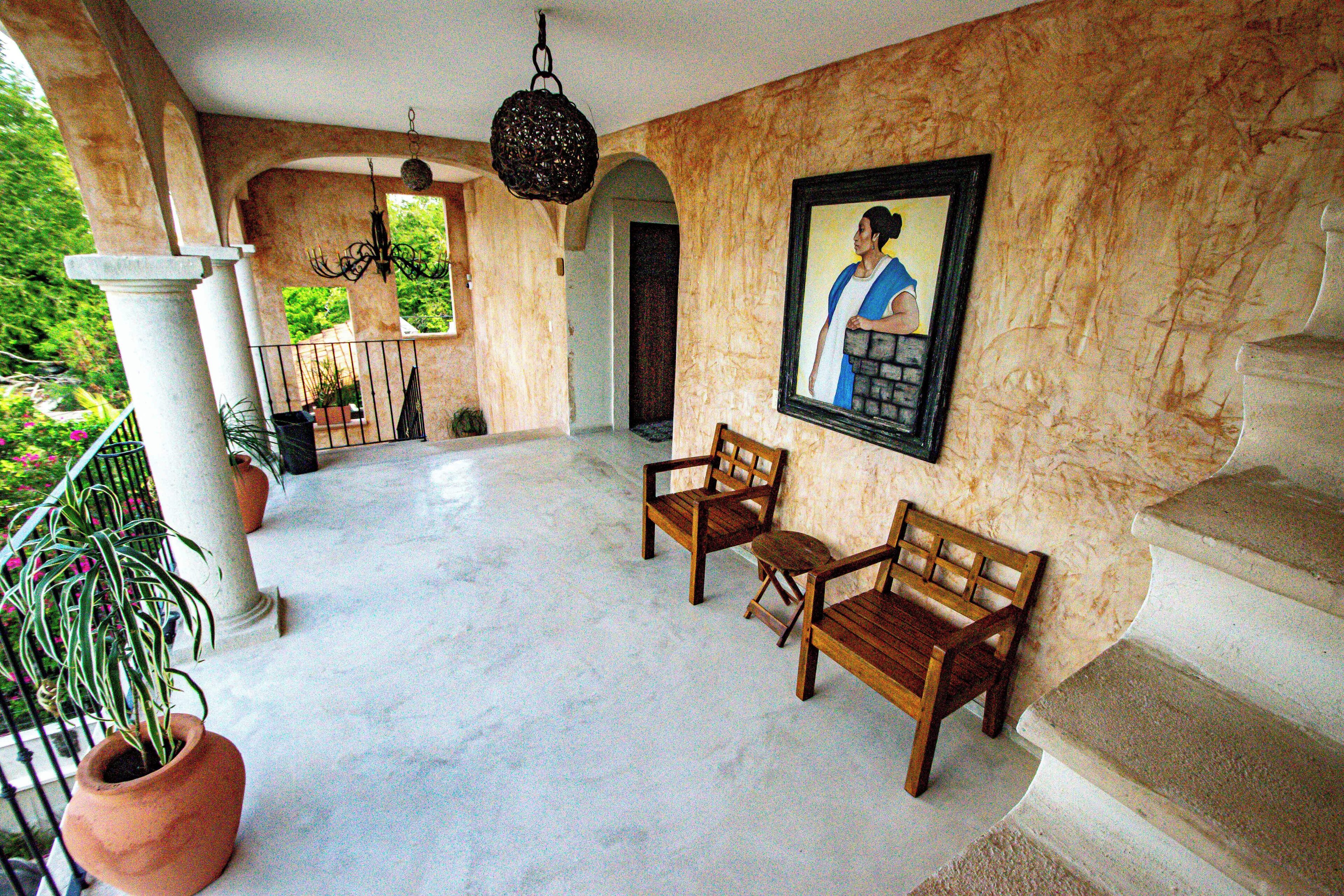 A spacious foyer with a marble floor, two wooden chairs, a potted plant, a hanging light fixture, and a framed portrait on the wall.