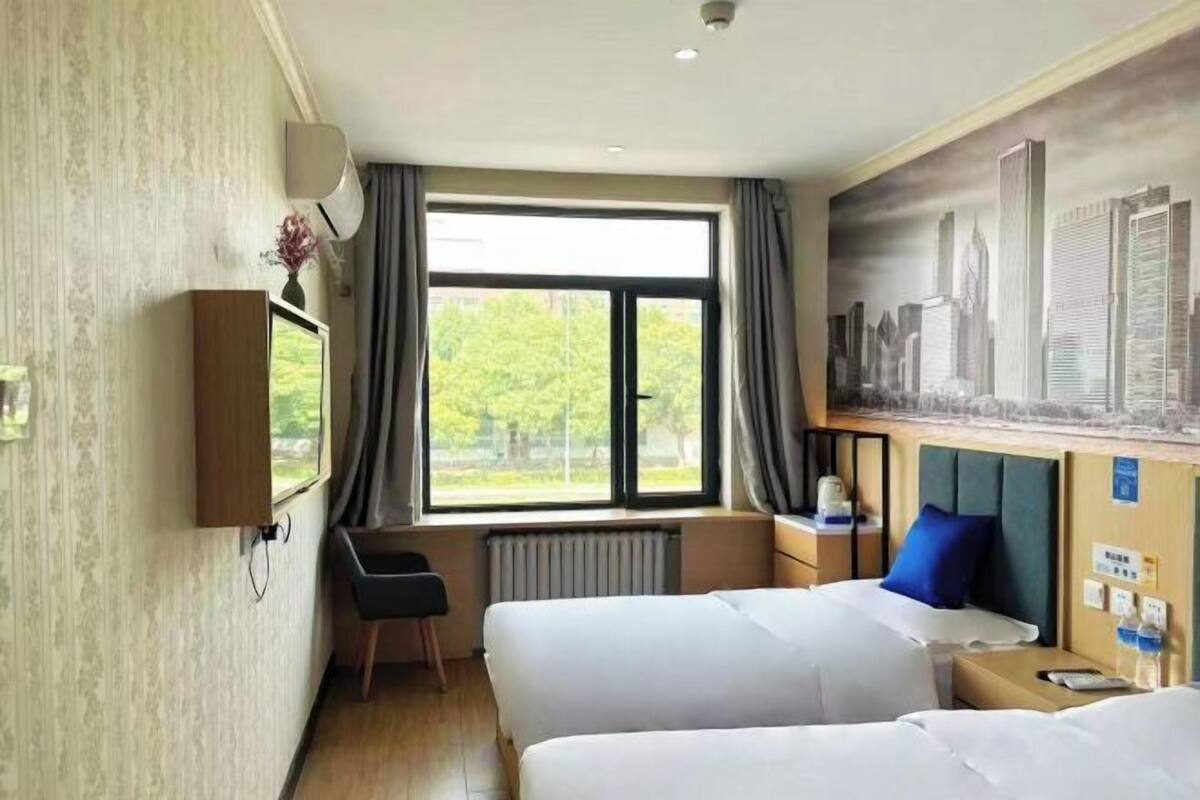 Een hotelkamer met twee bedden, een groot raam, een radiator, een bureau en een stadsgezicht muurschildering.