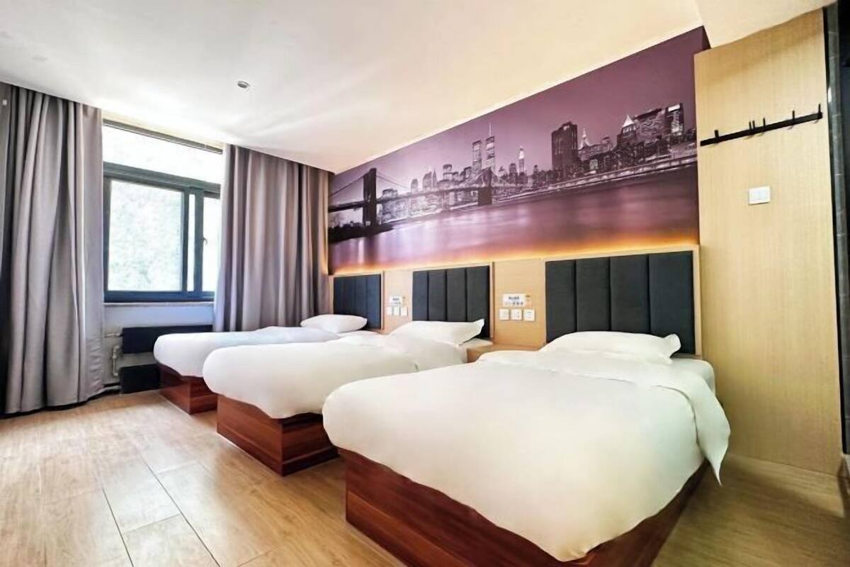 Een hotelkamer met twee bedden, een stadslandschap muurschildering, een raam met gordijnen en een houten vloer.