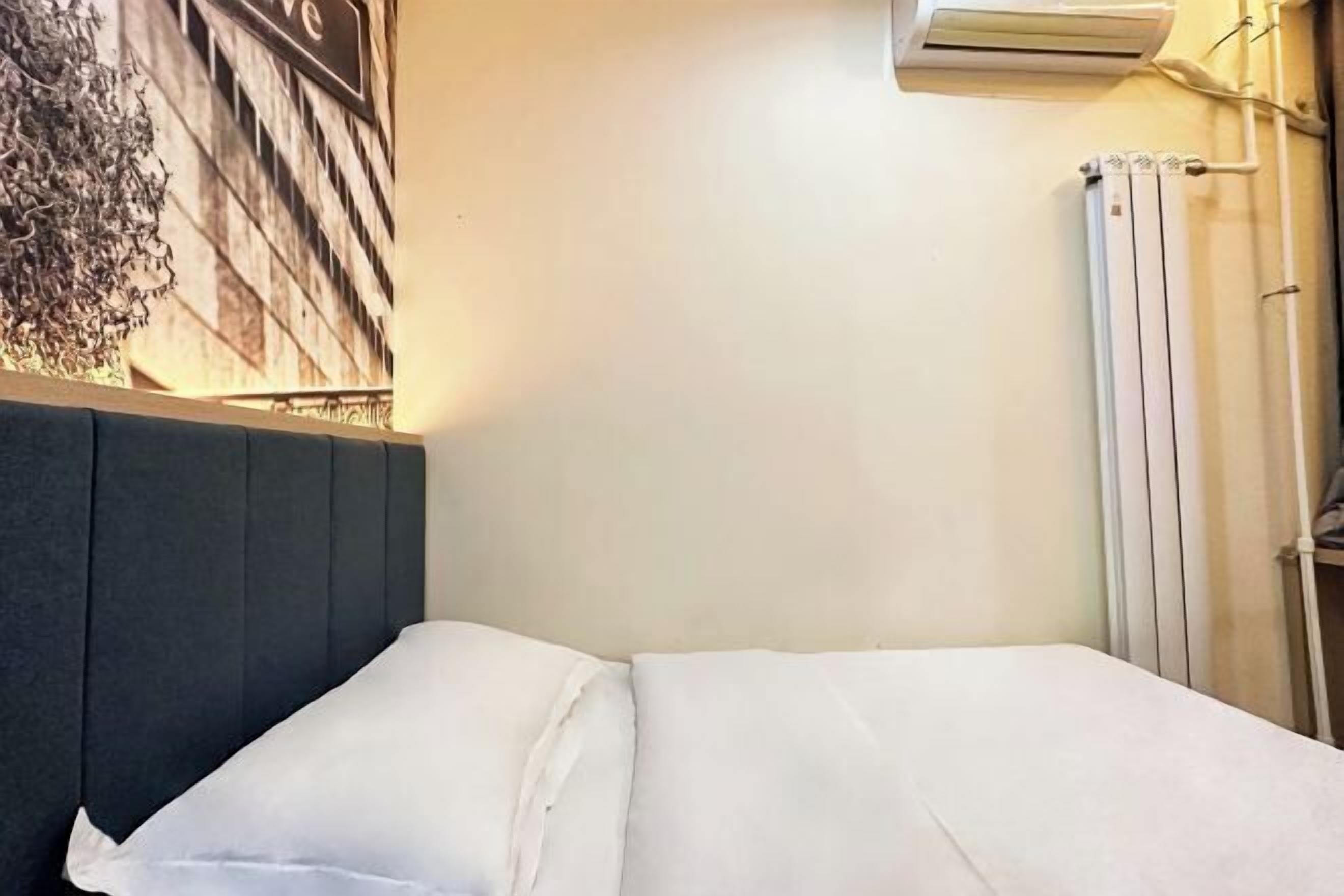 Een net opgemaakt bed met witte lakens in een kamer met een effen muur en een airconditioning er boven.